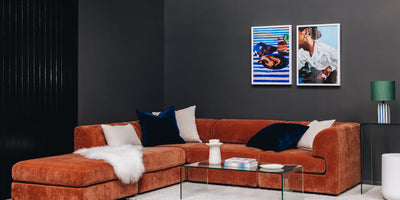 Modern living room with an orange sectional sofa, coffee table, and wall art.