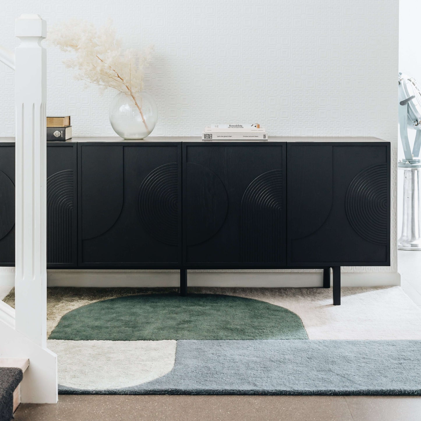 Modern black sideboard in a stylish living room with decorative vase and books on top, set on a geometric pattern rug.