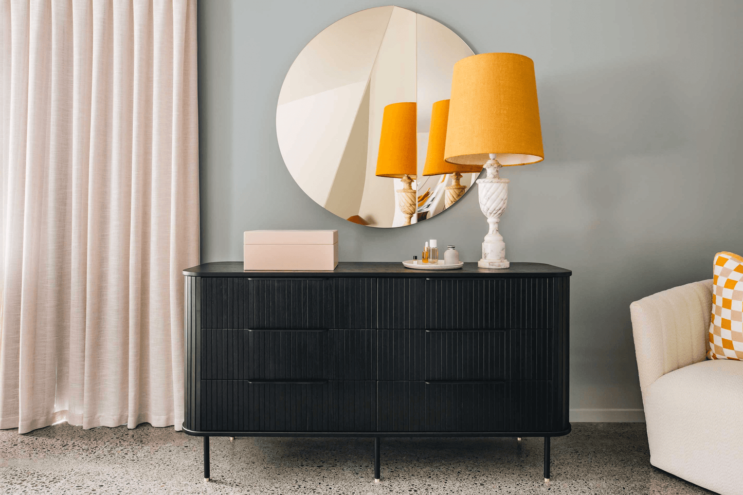 Modern dresser with a round mirror and orange lamp in a stylish living room setting