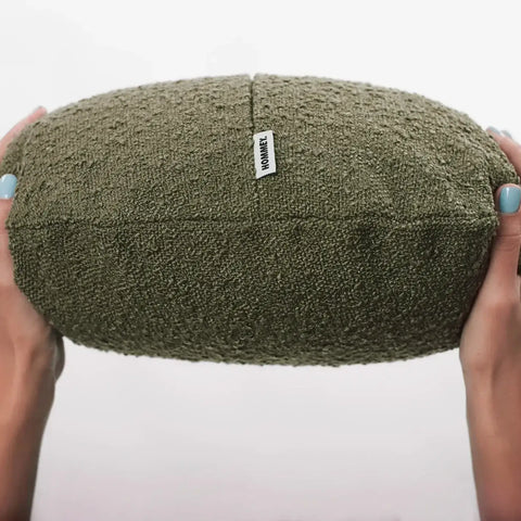 Person holding a textured green cushion with a label, showcasing cozy home decor.