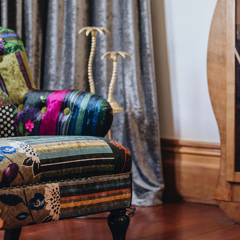 Patchwork armchair with velvet fabric and green buttons, styled in a room with curtains and a wooden cabinet, showcasing eclectic design.