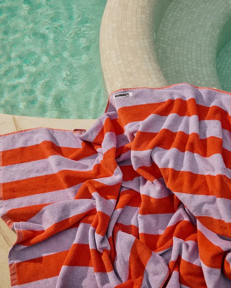 Luxurious Hommey grapefruit striped towel by the pool showcasing vibrant orange and purple stripes for a spa-like home experience.