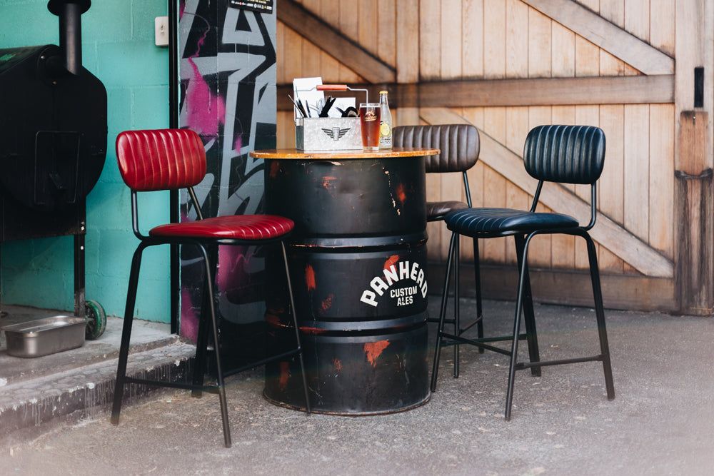 Retro Datsun Bar Stools in red and black, featuring vintage PU leather and industrial design, set around a rustic table outdoors.